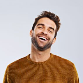 studio shot of a happy and handsome man laughing against a gray background.